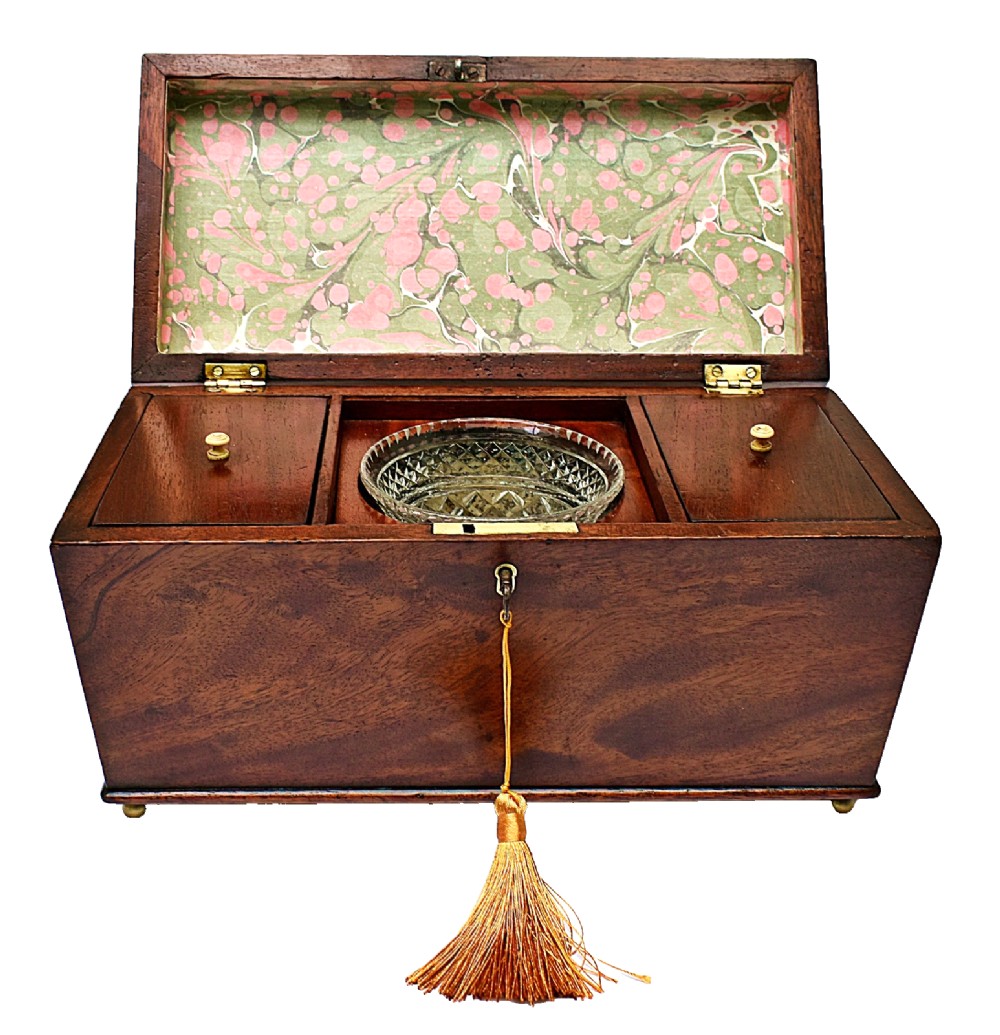 An open Victorian mahogany sarcophagus-shaped tea caddy featuring two lidded compartments, a central cut glass mixing bowl, marbled paper lid lining, and a key with a golden tassel.