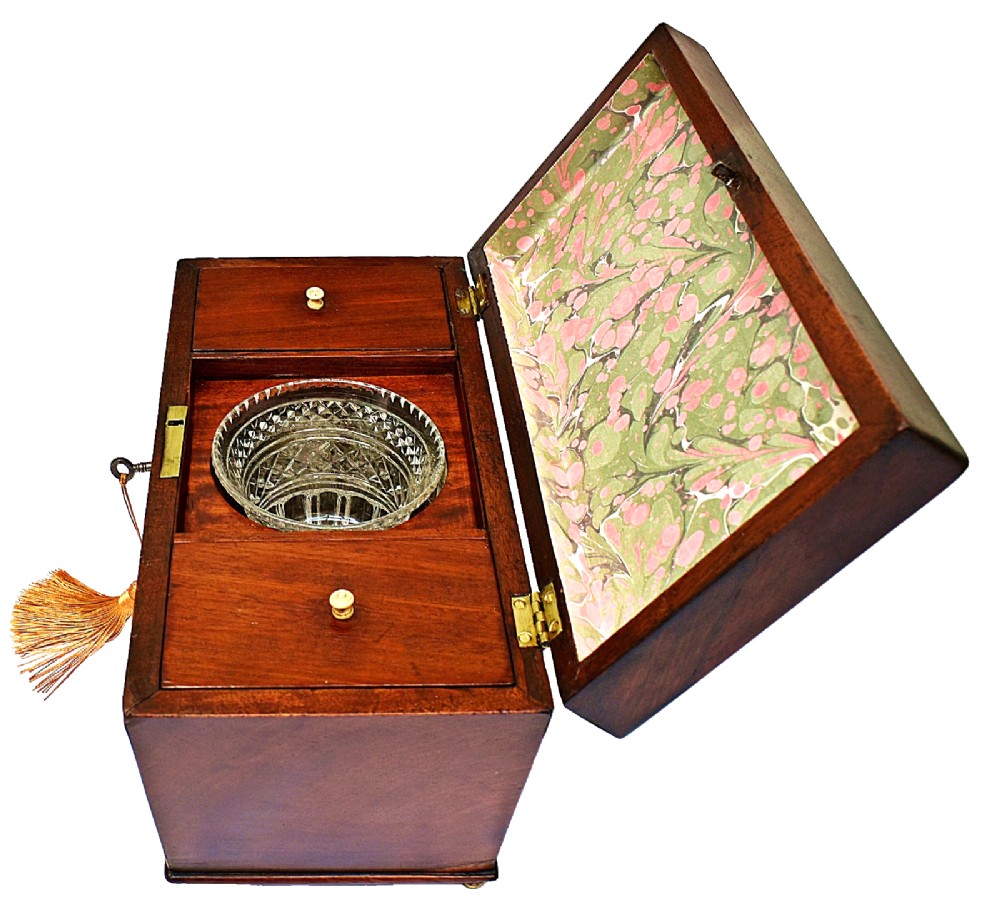 An open Victorian mahogany sarcophagus-shaped tea caddy featuring two lidded compartments, a central cut glass mixing bowl, marbled paper lid lining, and a key with a golden tassel. View IV