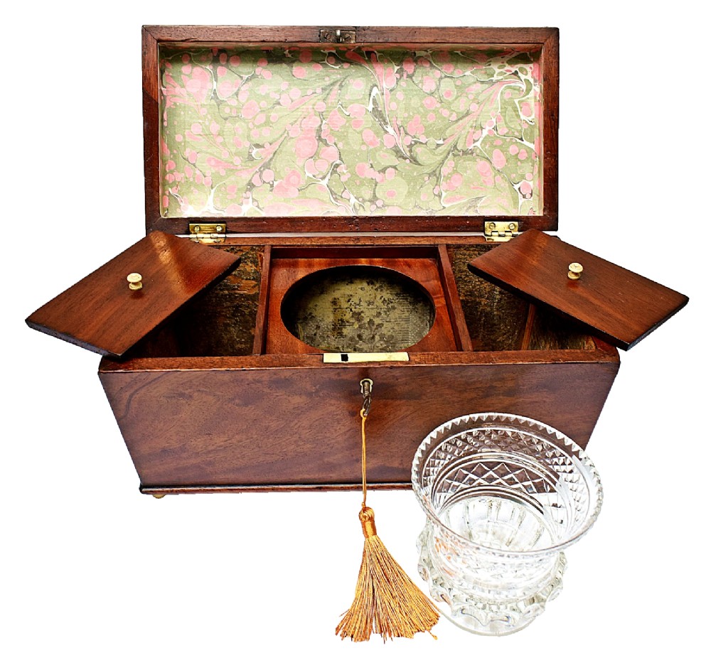 An open Victorian mahogany sarcophagus-shaped tea caddy featuring two lidded compartments, a central cut glass mixing bowl, marbled paper lid lining, and a key with a golden tassel. View X