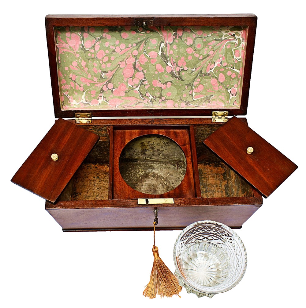 An open Victorian mahogany sarcophagus-shaped tea caddy featuring two lidded compartments, a central cut glass mixing bowl, marbled paper lid lining, and a key with a golden tassel. View XI