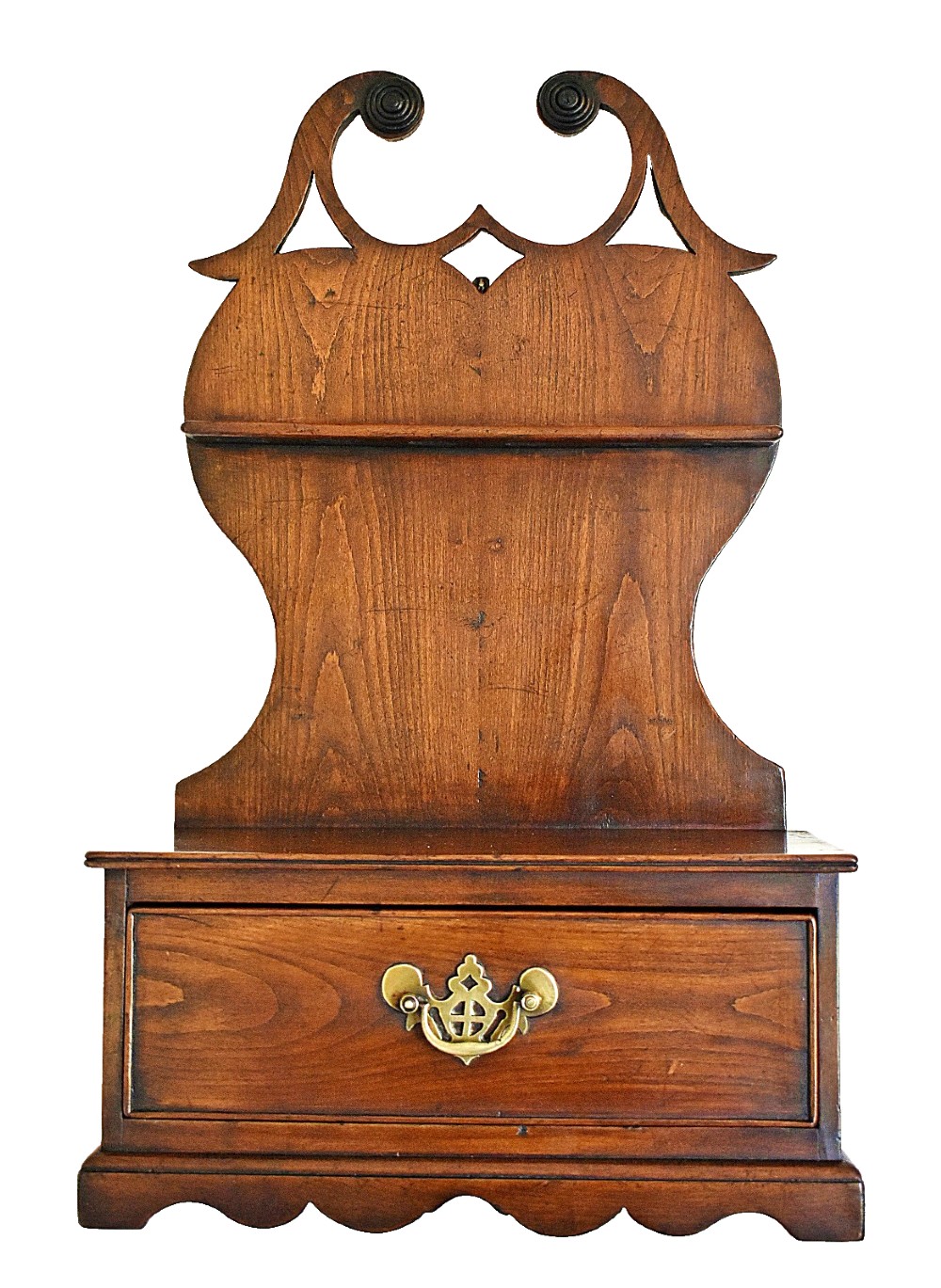 An antique carved oak spoon rack features a shaped scroll crest, a slotted rack, and a lower drawer with a brass drop handle.
