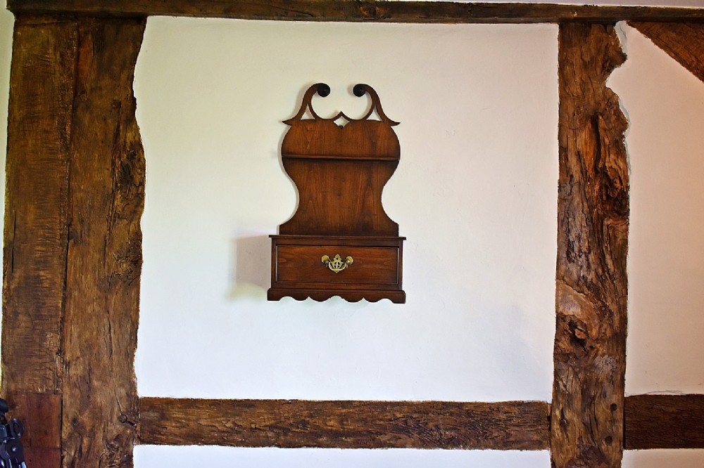 An antique carved oak spoon rack features a shaped scroll crest, a slotted rack, and a lower drawer with a brass drop handle. View II