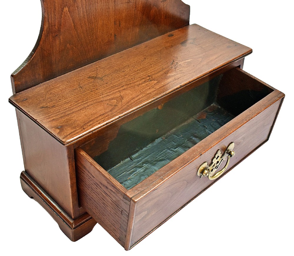 An antique carved oak spoon rack features a shaped scroll crest, a slotted rack, and a lower drawer with a brass drop handle. View IX