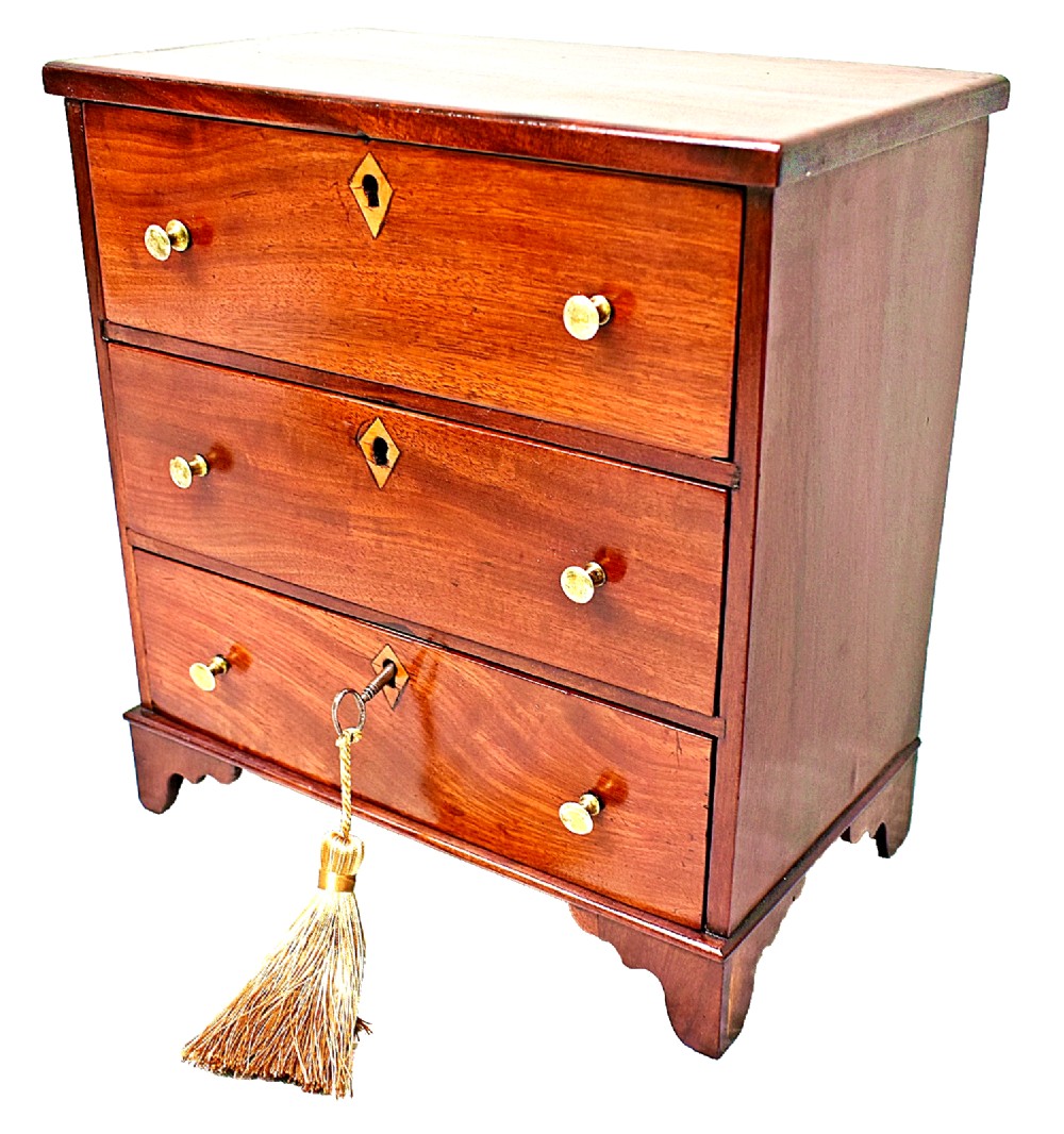 A Regency period miniature mahogany chest featuring three stacked drawers, small brass knobs, diamond escutcheons, shaped bracket feet, and a key with a tassel. View II
