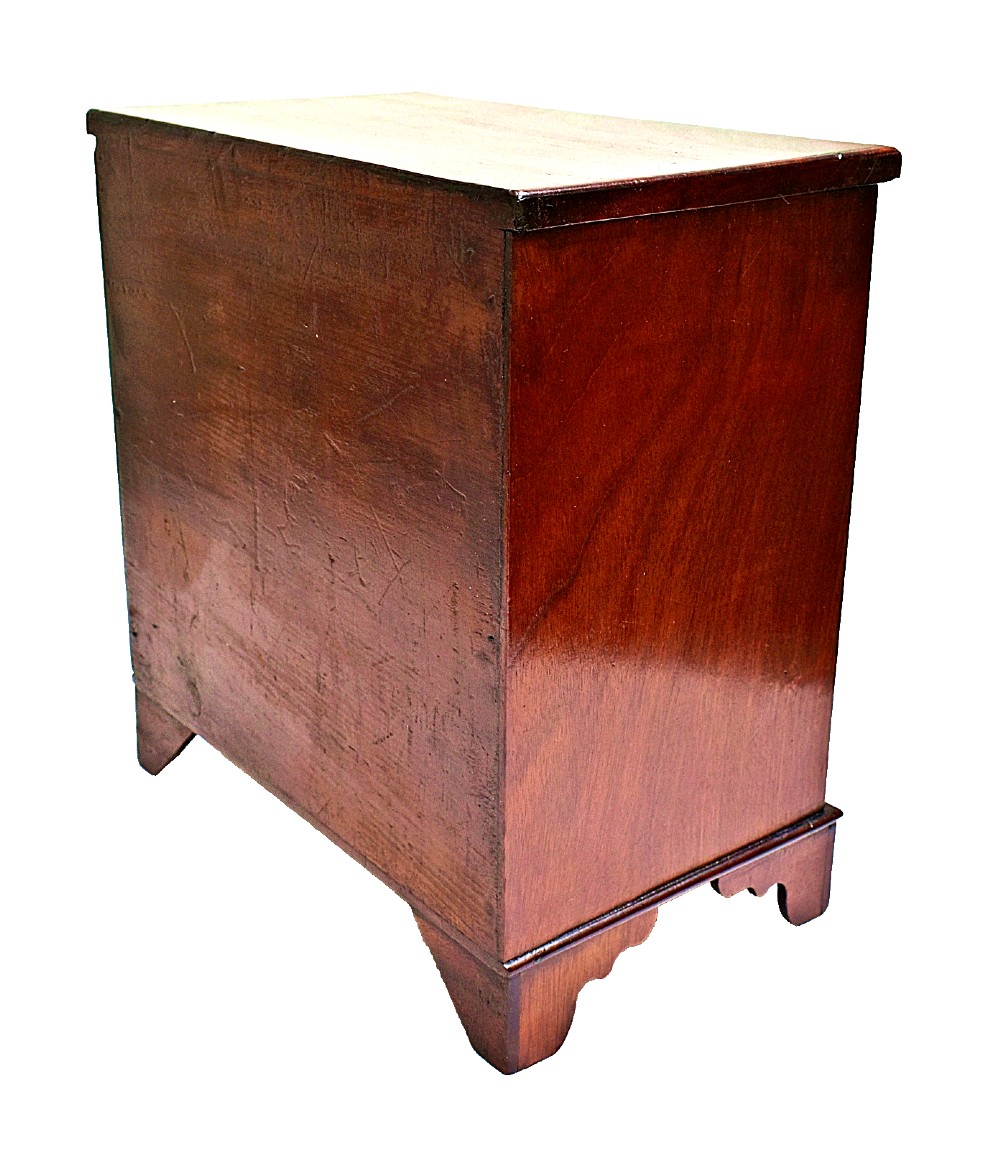 A Regency period miniature mahogany chest featuring three stacked drawers, small brass knobs, diamond escutcheons, shaped bracket feet, and a key with a tassel. View V