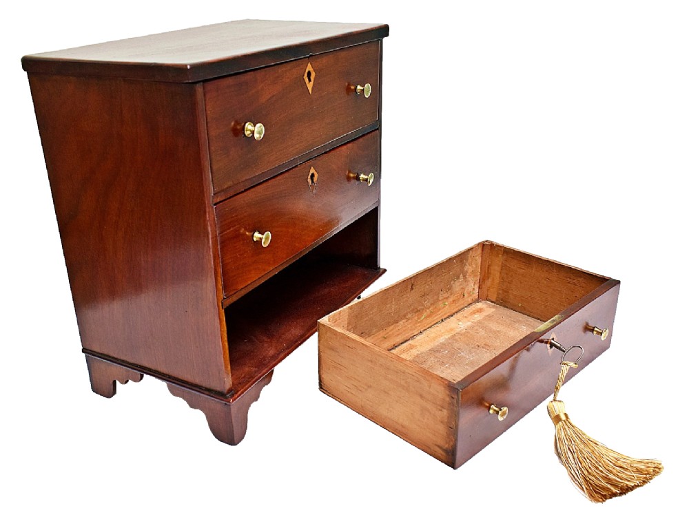 A Regency period miniature mahogany chest featuring three stacked drawers, small brass knobs, diamond escutcheons, shaped bracket feet, and a key with a tassel. View VII