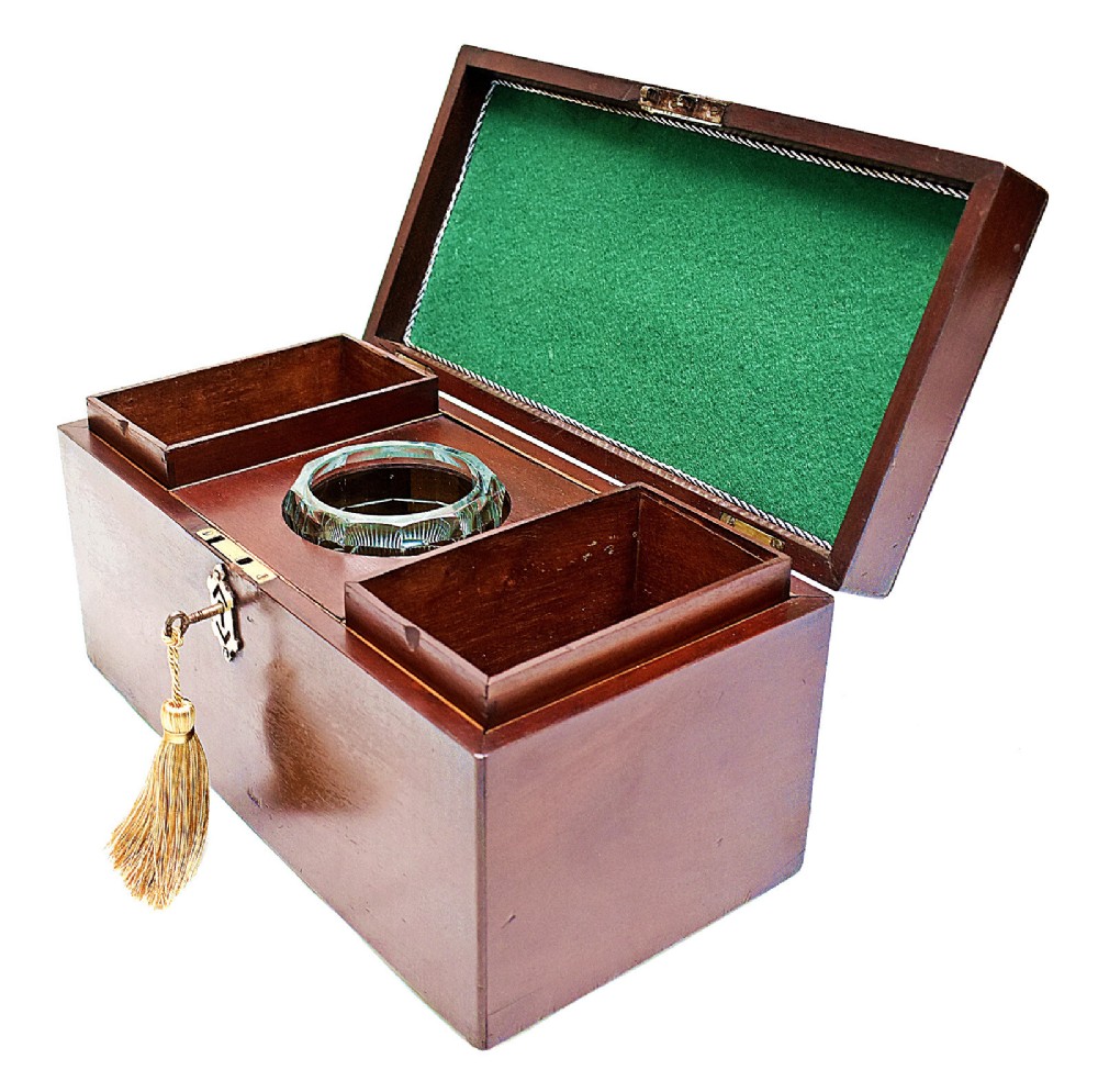 An open rectangular dark wood tea caddy featuring two internal covered compartments, a central cut glass mixing bowl, a green fabric-lined lid, and a key with a tassel inserted in the front lock.