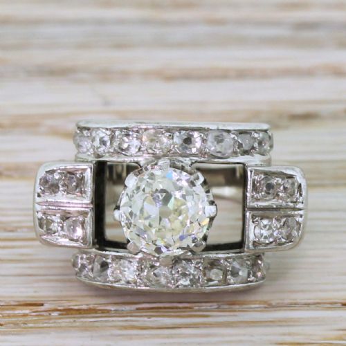 fig 1. An Art Deco diamond ring featuring a central round old European cut diamond set within an architectural rectangular metal frame surrounded by accent diamonds.