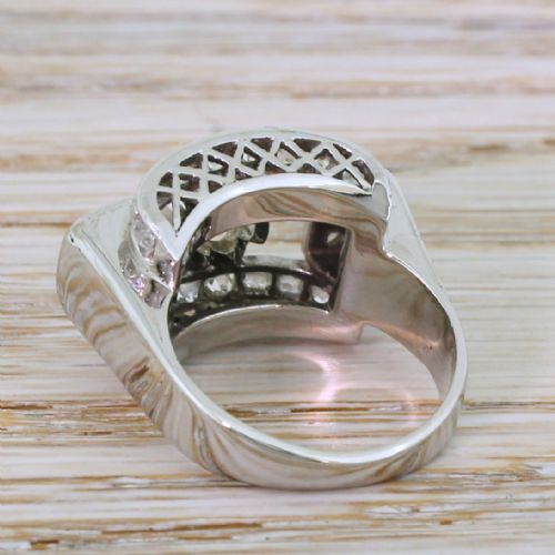 fig 3. An Art Deco diamond ring featuring a central round old European cut diamond set within an architectural rectangular metal frame surrounded by accent diamonds.