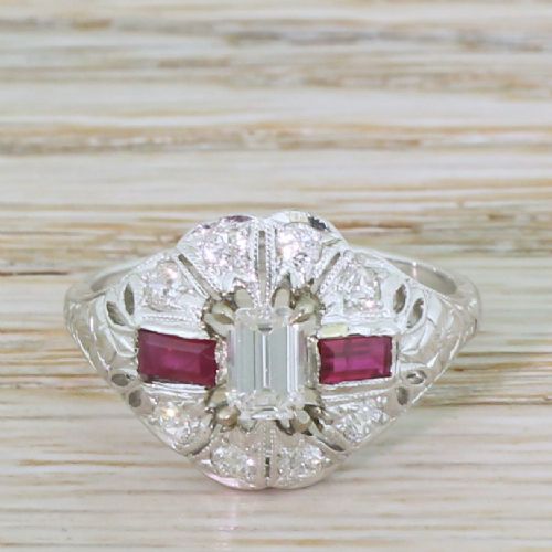 fig 1. A retro silver-tone ring featuring a central emerald-cut diamond flanked by two rectangular rubies surrounded by pierced filigree work.
