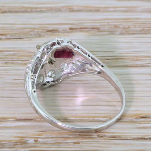 fig 3. A retro silver-tone ring featuring a central emerald-cut diamond flanked by two rectangular rubies surrounded by pierced filigree work.