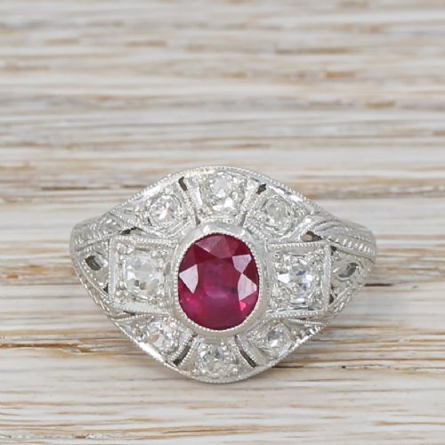 fig 1. An Art Deco platinum ring featuring a central oval red ruby framed by old cut diamonds within a geometric pierced setting with engraved shoulders.