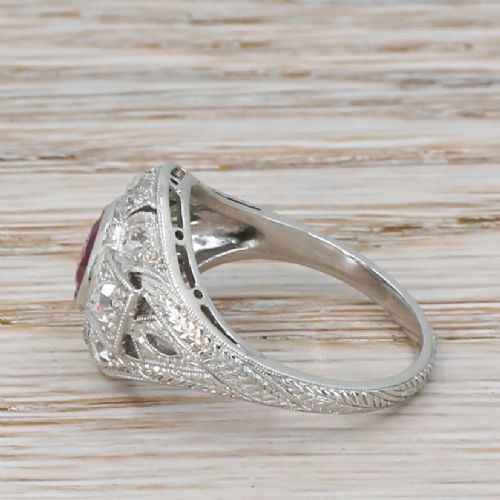 fig 2. An Art Deco platinum ring featuring a central oval red ruby framed by old cut diamonds within a geometric pierced setting with engraved shoulders.