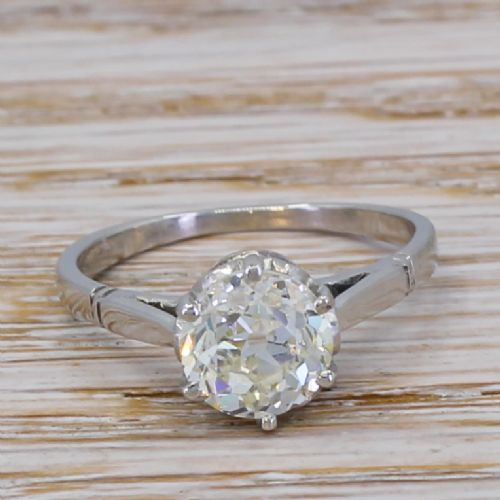fig 1. An Art Deco solitaire ring featuring a round old cut diamond held in a six-prong setting with tapered geometric shoulders crafted in white metal.