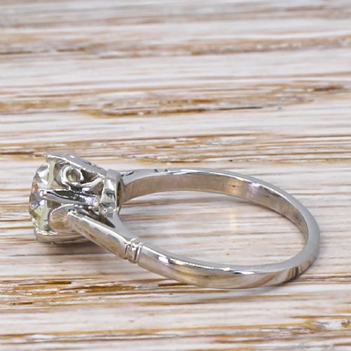 fig 2. An Art Deco solitaire ring featuring a round old cut diamond held in a six-prong setting with tapered geometric shoulders crafted in white metal.