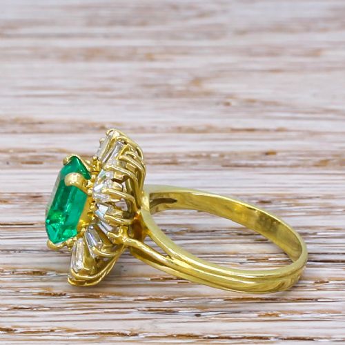 fig 2. A yellow gold ballerina ring featuring a central rectangular emerald cut green emerald surrounded by a flared halo of baguette diamonds.