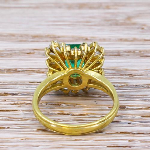 fig 3. A yellow gold ballerina ring featuring a central rectangular emerald cut green emerald surrounded by a flared halo of baguette diamonds.