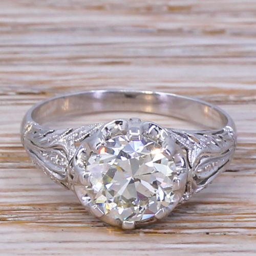 fig 1. A mid-century solitaire ring featuring a central round old-cut diamond set in a multi-claw platinum mounting with carved foliate shoulder details.
