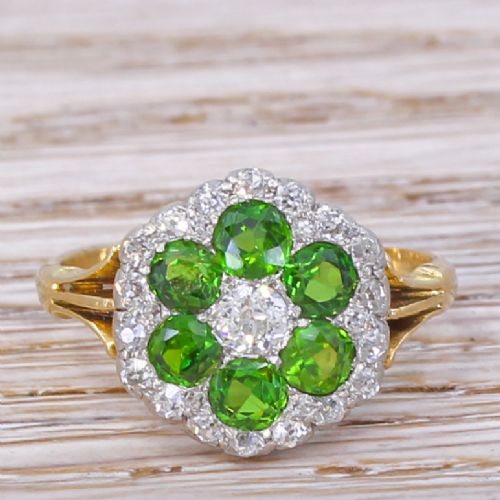 fig 1. An Edwardian flower cluster ring featuring six round green demantoid garnets and a central diamond, framed by small diamond accents in a yellow gold setting.