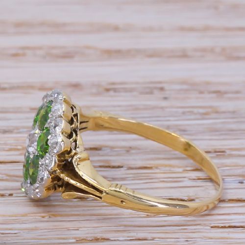 fig 2. An Edwardian flower cluster ring featuring six round green demantoid garnets and a central diamond, framed by small diamond accents in a yellow gold setting.