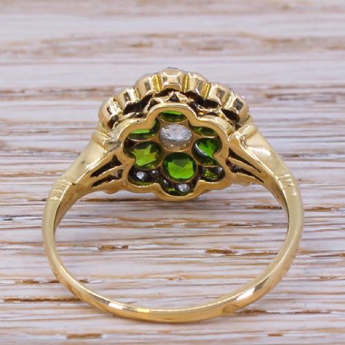 fig 3. An Edwardian flower cluster ring featuring six round green demantoid garnets and a central diamond, framed by small diamond accents in a yellow gold setting.
