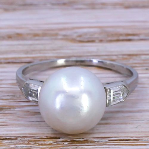 fig 1. An Art Deco solitaire ring displaying a round white natural pearl flanked by geometric shoulder diamonds set in a platinum band.