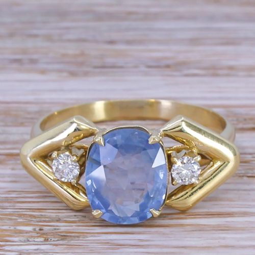 fig 1. A yellow gold ring featuring a central oval-cut light blue sapphire flanked by two round diamonds within geometric gold shoulders.