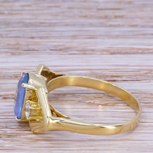 fig 2. A yellow gold ring featuring a central oval-cut light blue sapphire flanked by two round diamonds within geometric gold shoulders.