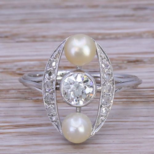 fig 1. A mid-century platinum dress ring featuring a central bezel-set round diamond flanked vertically by two white pearls inside an openwork oval diamond-set frame.