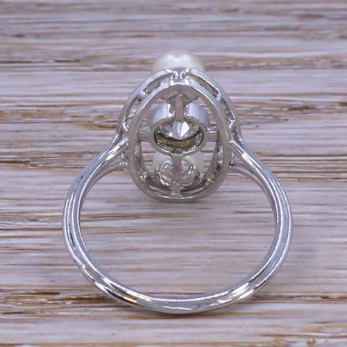 fig 3. A mid-century platinum dress ring featuring a central bezel-set round diamond flanked vertically by two white pearls inside an openwork oval diamond-set frame.