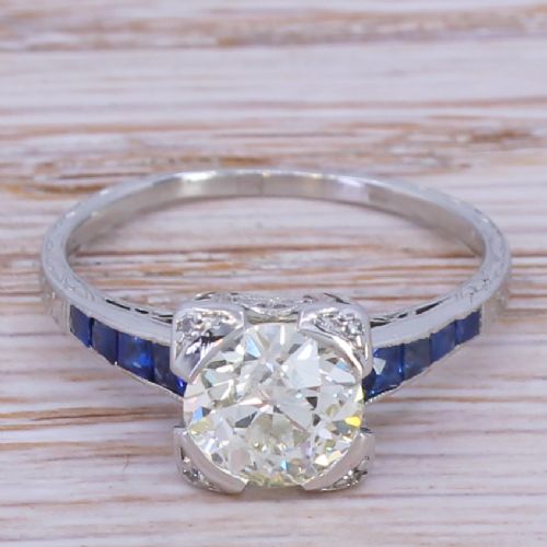 fig 1. An Art Deco diamond solitaire ring set in white metal featuring calibre-cut sapphire shoulders and engraved metalwork.
