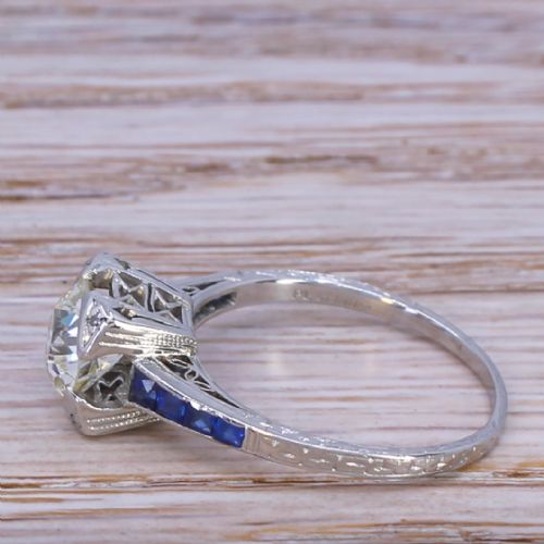 fig 2. An Art Deco diamond solitaire ring set in white metal featuring calibre-cut sapphire shoulders and engraved metalwork.