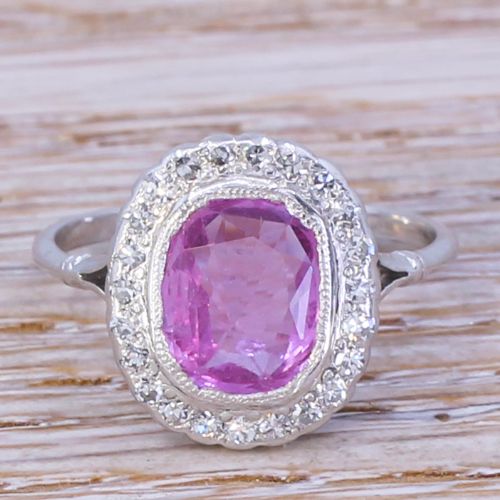fig 1. A mid-century ring featuring a central cushion-cut pink sapphire framed by a halo of small diamonds set in a white metal band with split shoulders.