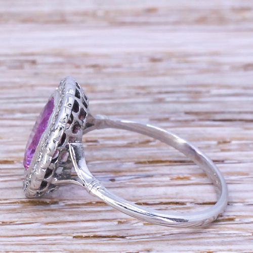 fig 2. A mid-century ring featuring a central cushion-cut pink sapphire framed by a halo of small diamonds set in a white metal band with split shoulders.