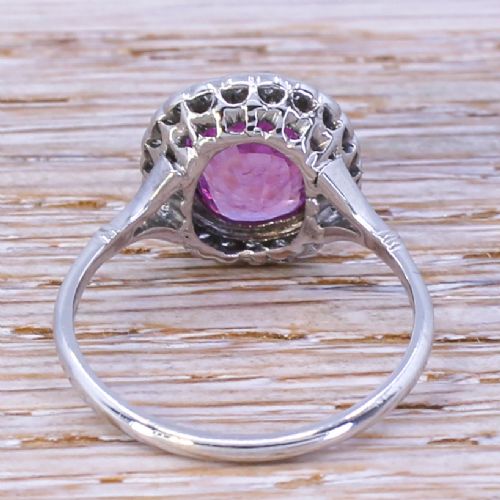 fig 3. A mid-century ring featuring a central cushion-cut pink sapphire framed by a halo of small diamonds set in a white metal band with split shoulders.