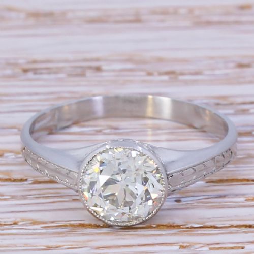 fig 1. An Art Deco platinum engagement ring featuring a central bezel-set old cut diamond with millgrain edging and engraved shoulder details.