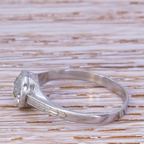 fig 2. An Art Deco platinum engagement ring featuring a central bezel-set old cut diamond with millgrain edging and engraved shoulder details.