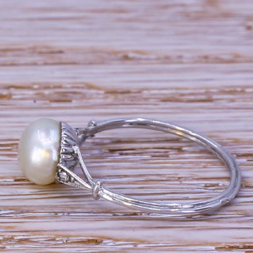 fig 2. A mid-century ring featuring a smooth, light cream natural pearl solitaire mounted on a slender silver-coloured band with subtle diamond accents on the shoulders.