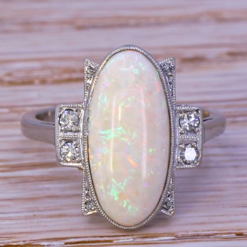fig 1. An Art Deco ring featuring a central oval opal cabochon flanked by geometric diamond-set stepped shoulders in a millegrain white metal setting.