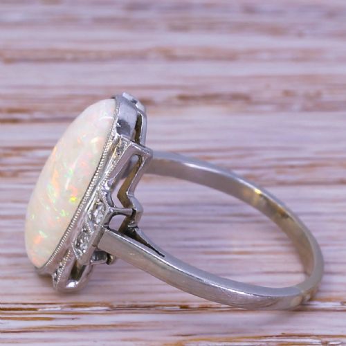fig 2. An Art Deco ring featuring a central oval opal cabochon flanked by geometric diamond-set stepped shoulders in a millegrain white metal setting.