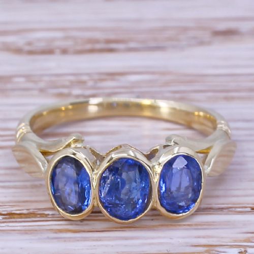 fig 1. A Victorian yellow gold trilogy ring featuring three oval-cut blue sapphires set in bezel mounts along a carved band.