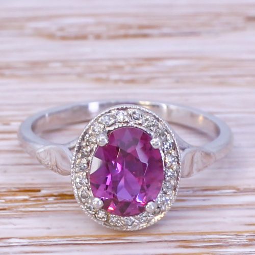 fig 1. An Art Deco ruby and diamond cluster ring featuring an oval cut red ruby framed by small diamonds on a silver-toned metal band.