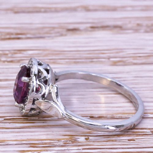 fig 2. An Art Deco ruby and diamond cluster ring featuring an oval cut red ruby framed by small diamonds on a silver-toned metal band.