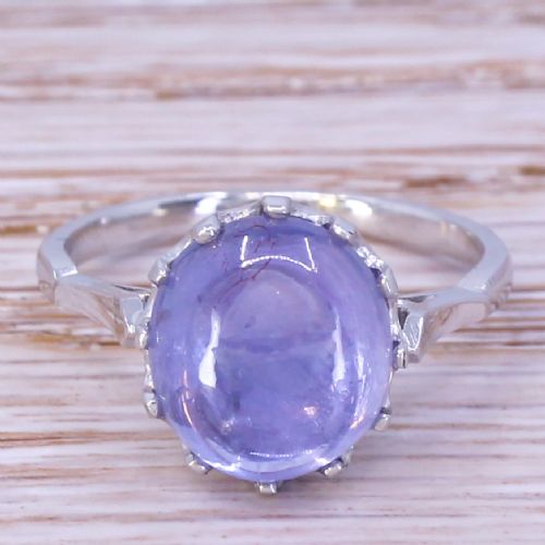 fig 1. An Art Deco ring featuring a smooth, oval purple cabochon sapphire held in a multi-claw metal setting on a slender band.