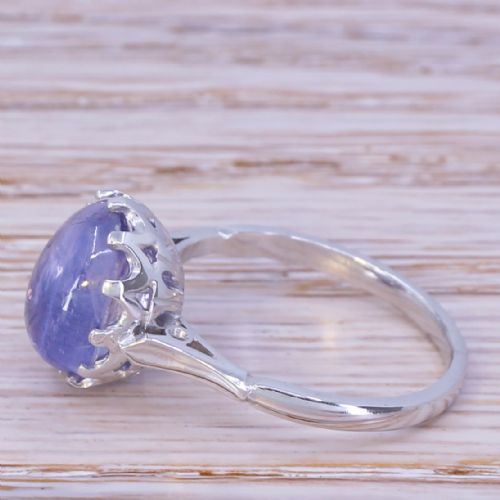 fig 2. An Art Deco ring featuring a smooth, oval purple cabochon sapphire held in a multi-claw metal setting on a slender band.