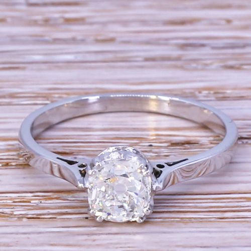 fig 1. An Art Deco diamond solitaire ring featuring an old cut diamond set in a polished silver-toned metal band with pierced shoulders.