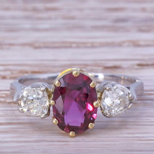 fig 1. An Art Deco three-stone ring featuring a central oval cut red ruby claw-set alongside two round diamonds on a silver-coloured metal band.