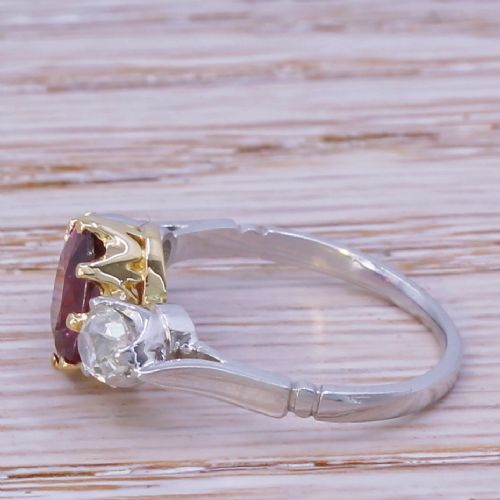 fig 2. An Art Deco three-stone ring featuring a central oval cut red ruby claw-set alongside two round diamonds on a silver-coloured metal band.