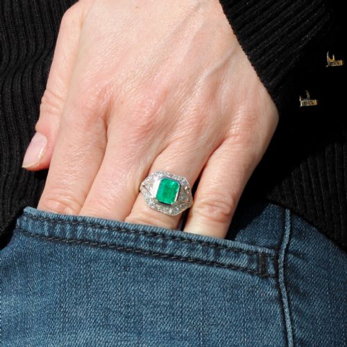 fig 1. An Art Deco platinum ring featuring a central rectangular green emerald surrounded by a geometric halo of white diamonds with milgrain detailing.
