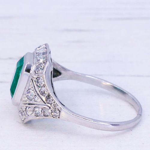 fig 3. An Art Deco platinum ring featuring a central rectangular green emerald surrounded by a geometric halo of white diamonds with milgrain detailing.